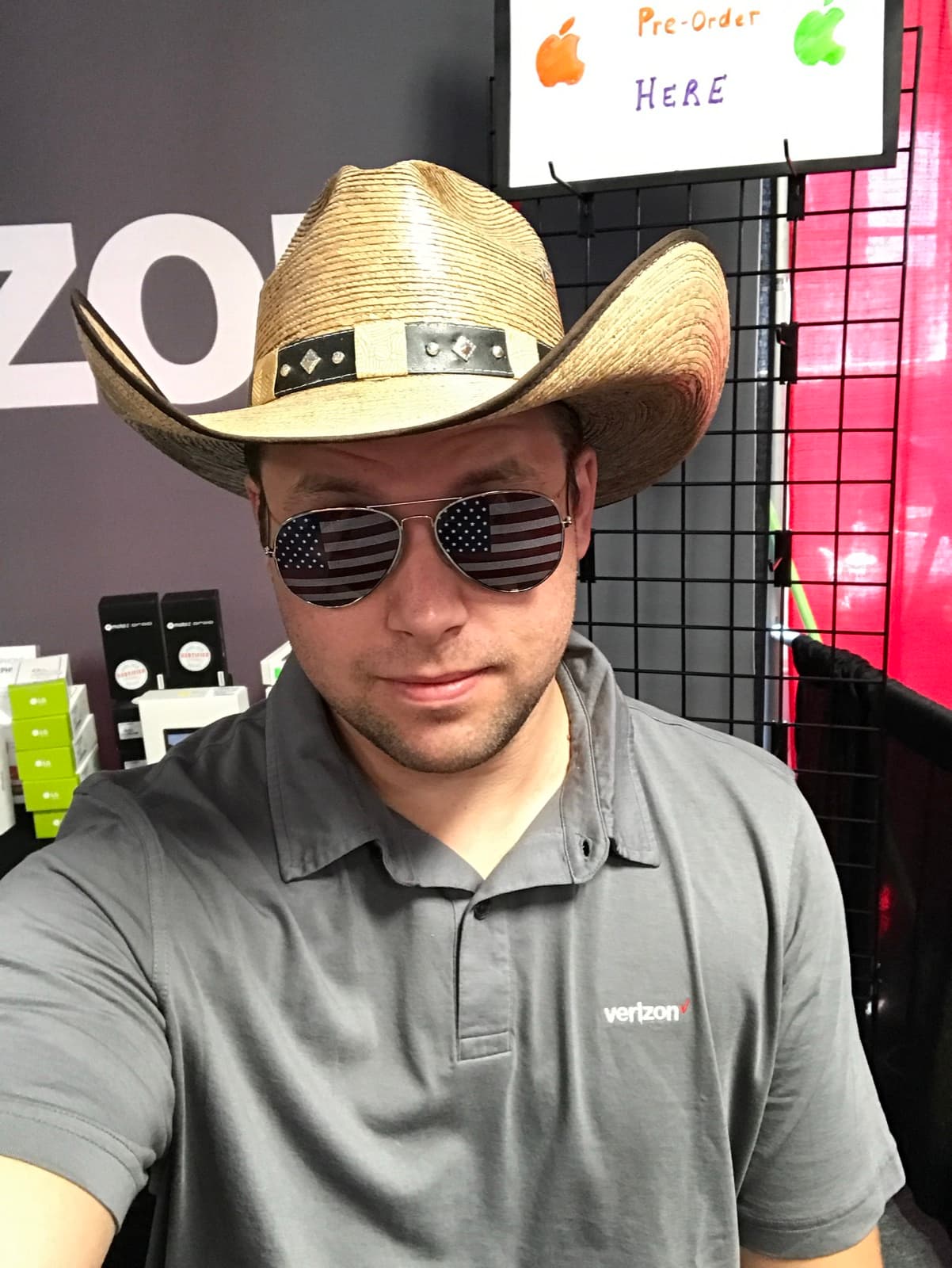 Jeremy Gulley in a Verizon polo shirt, straw cowboy hat and American-flag aviator sunglasses, on the floor of a Verizon retail store